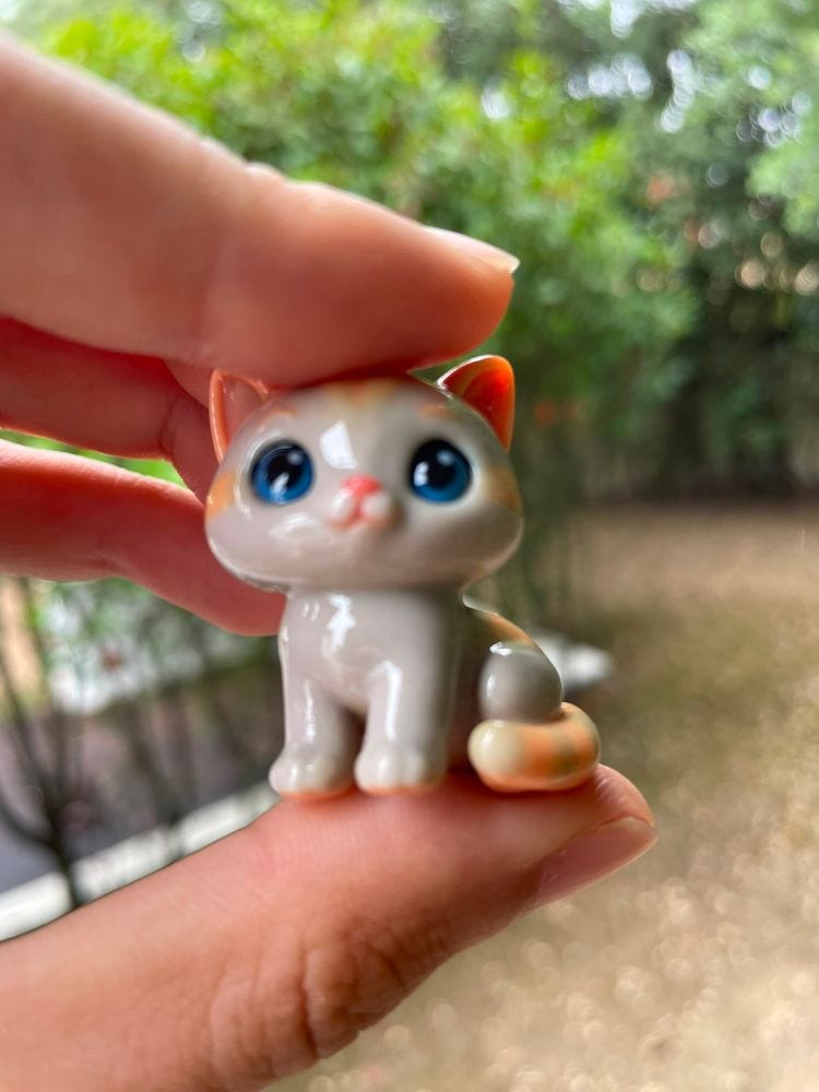 Ginger-and-white kitten keychain held between two fingers in a garden