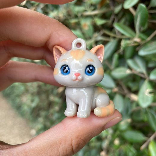 Miniature ginger-and-white kitten charm held between two fingers